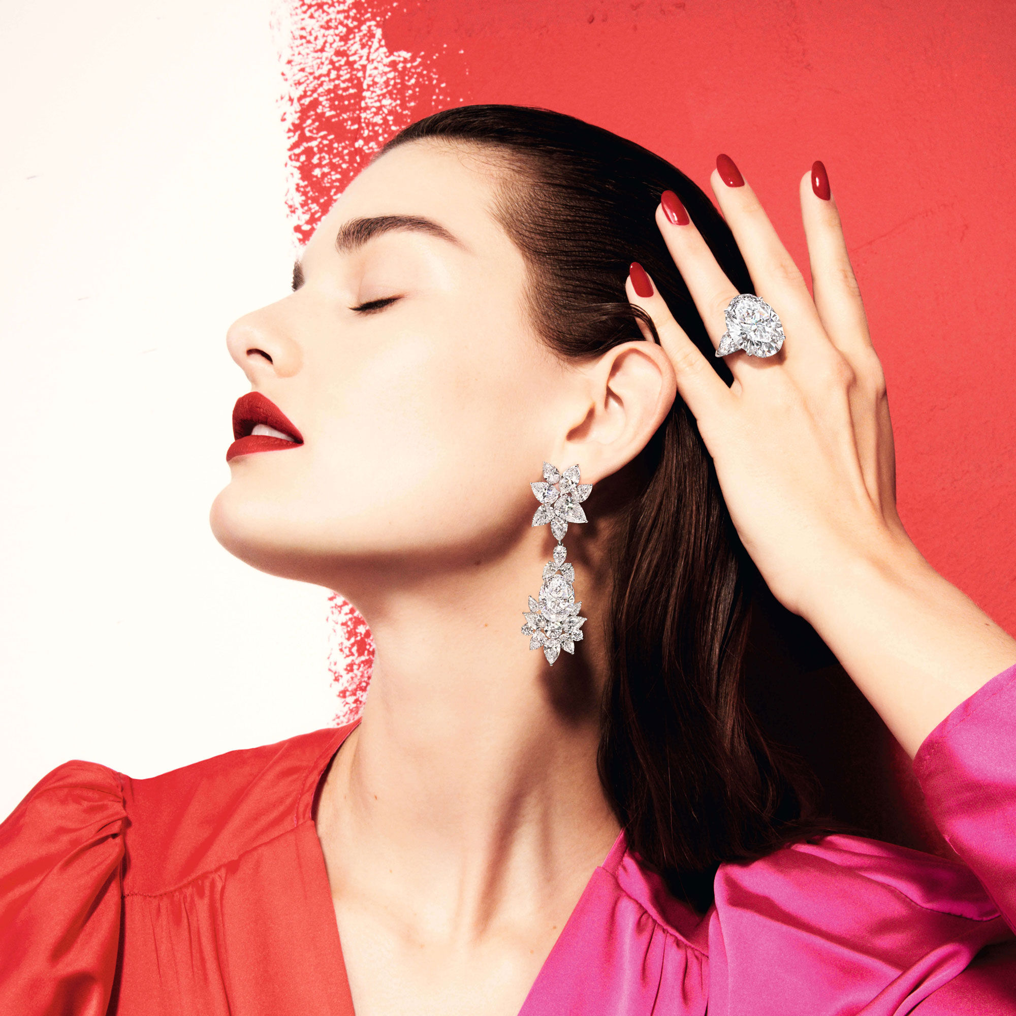 close up of a lady standing in front of a wall with red paint wearing Graff diamond earrings and ring