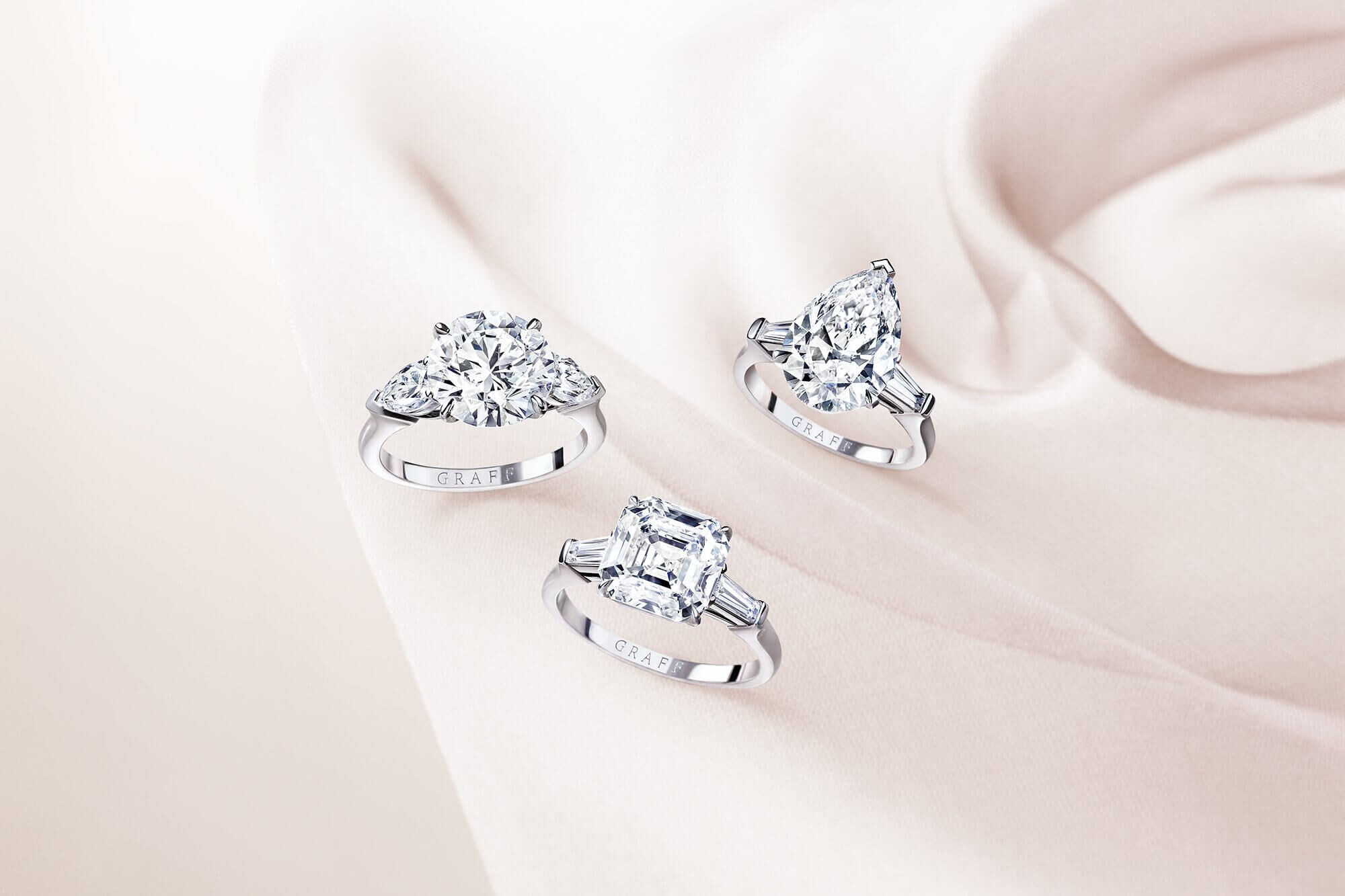 Three promise diamond engagement rings by Graff on a silk fabric