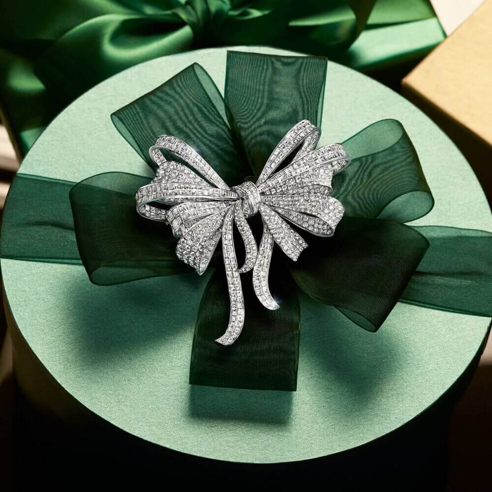 A Graff Diamond Bow Brooch on a holiday season christmas green gift box placed on a piano next to other gift boxes