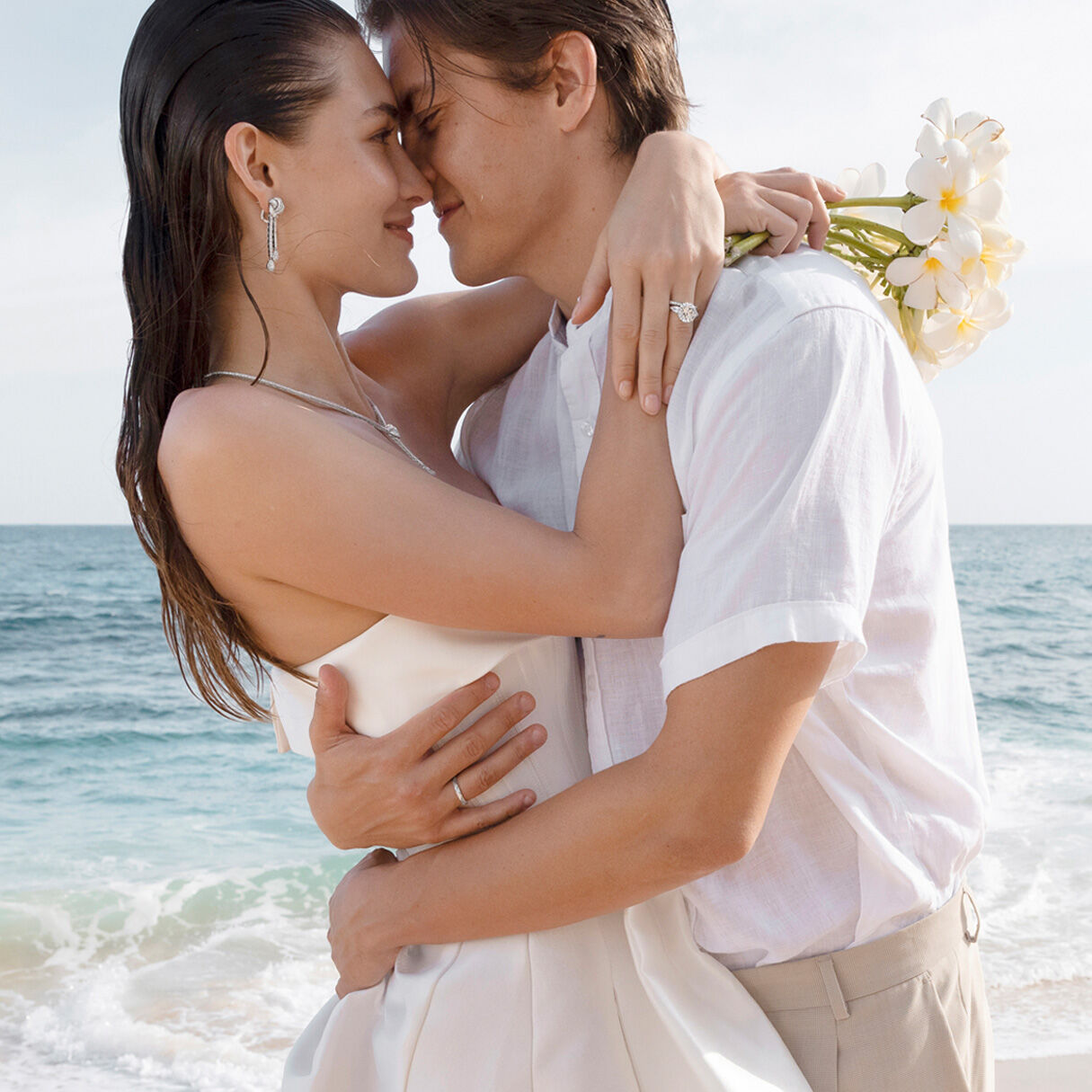 Graff bride and groom on beach, female model wearing Graff Diamond engagement ring and wedding band and Graff Tilda's Bow Jewellery Suite
