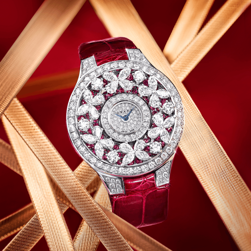 A Graff Classic Butterfly Diamond on Ruby Watch with red leather Strap on a red background with gold ribbons