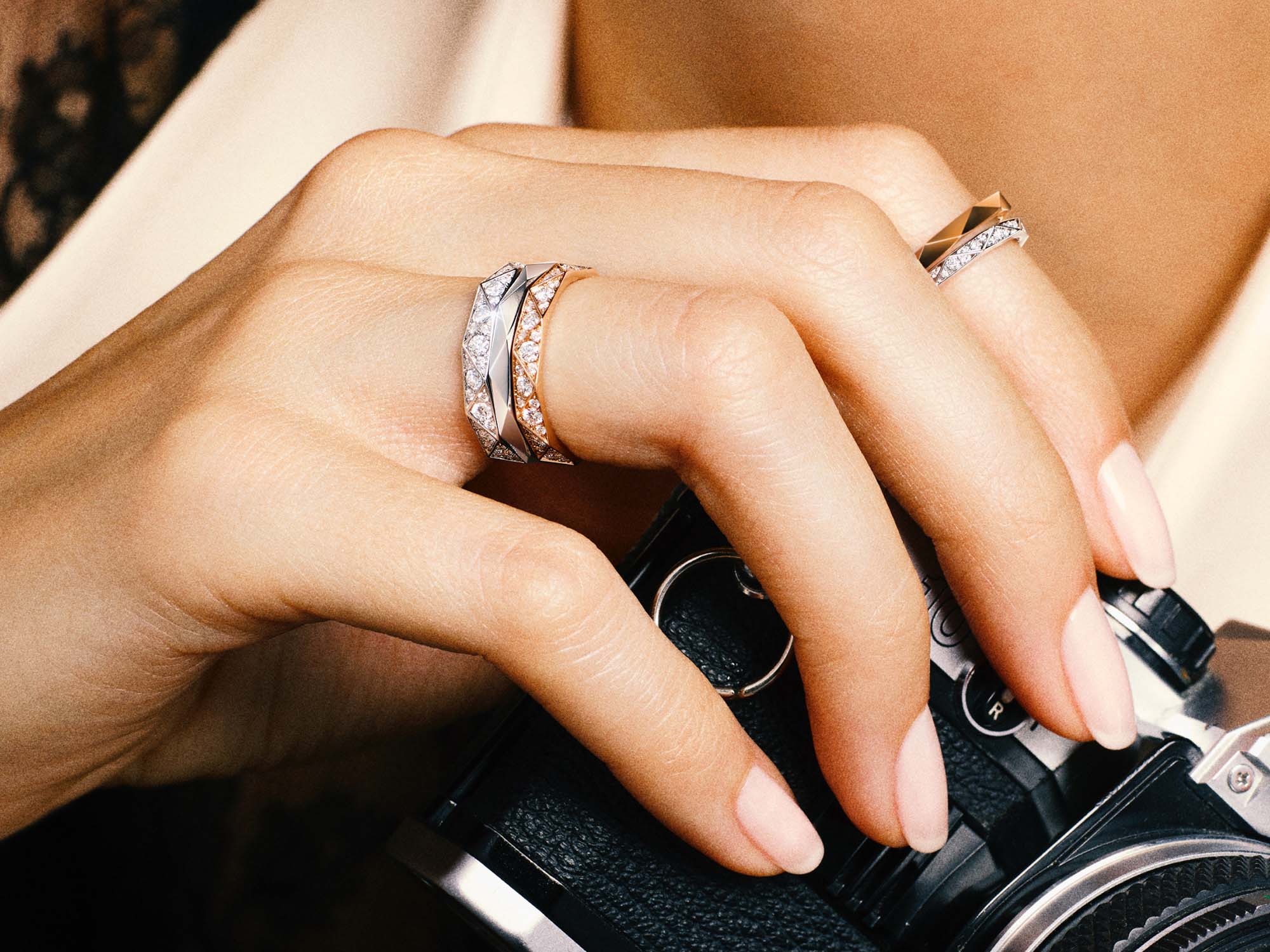 Model holding camera and wearing Laurence Graff signature bands, white gold and rose gold pave and rose gold plain.